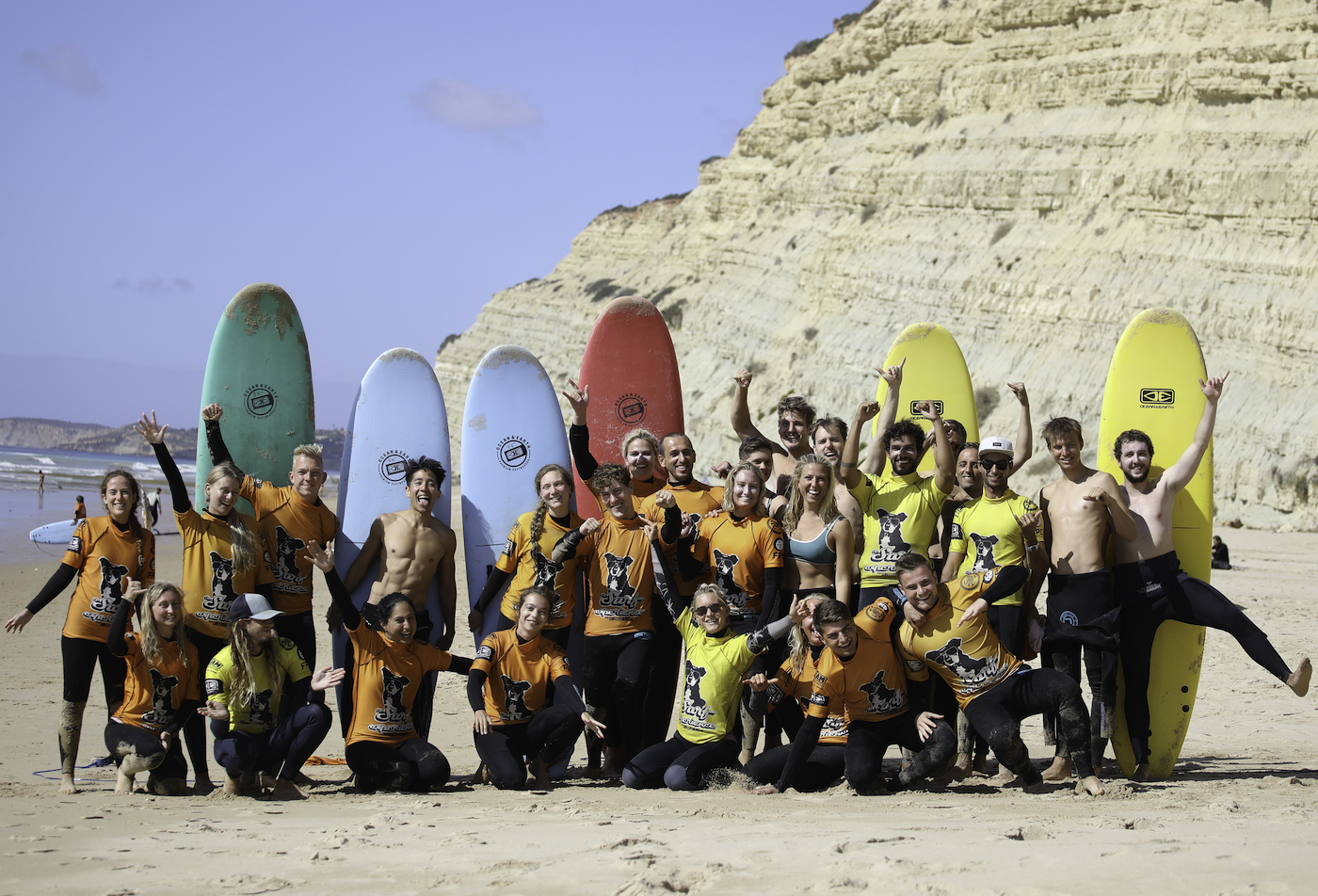 A summer surf group with The Surf Experience. A big group of people stood in front of surf boards, all laughing and joking.