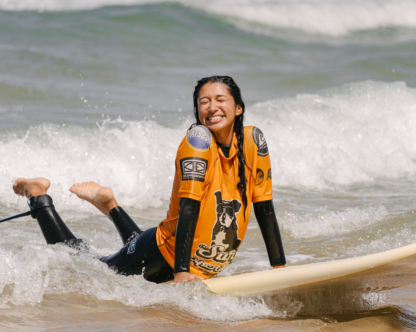 A girl surfing a wave on her hands and knees on a surfboard on a summer trip with The Surf Experience. She has a big smile on her face.