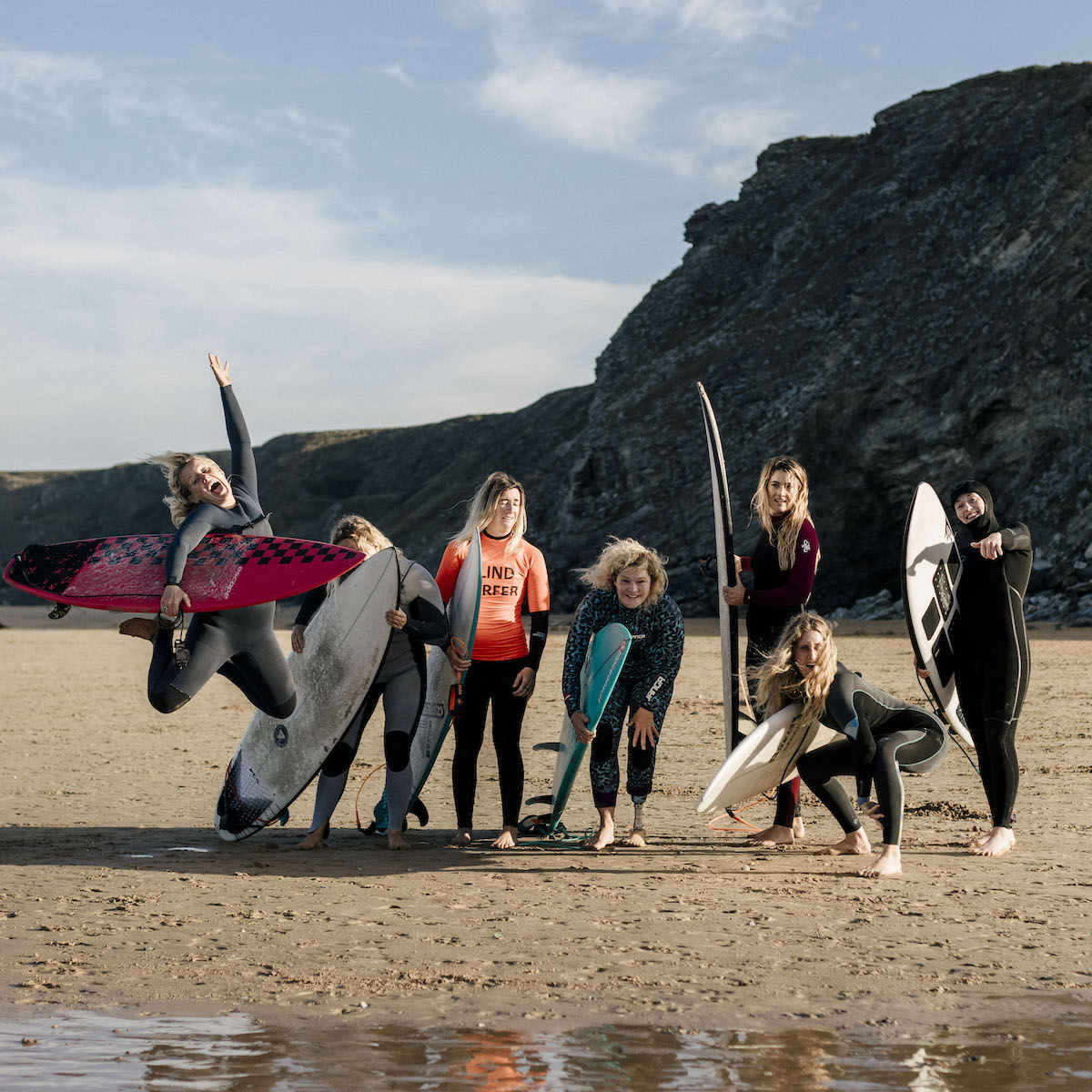 Summer Surf with Gather and Glide. 7 ladies holding surfboards, doing different poses, like jumping in the air and kneeling down. 
