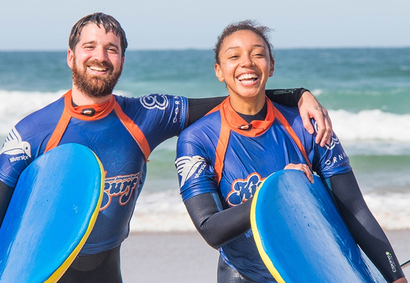 2 customers smiling and holding surfboards at their surf lesson with Kingsurf - one of Cornwall's surf schools
